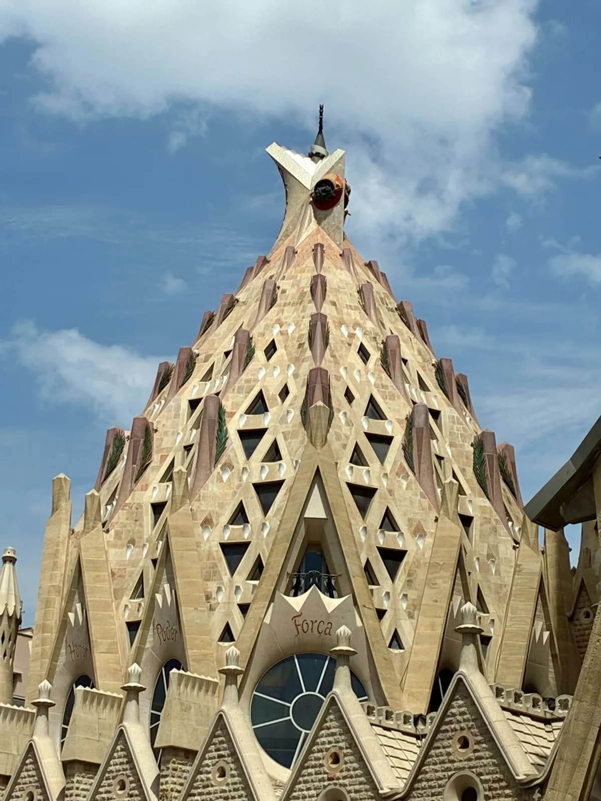 Upper section of a Sagrada Família tower beneath a cloudy sky